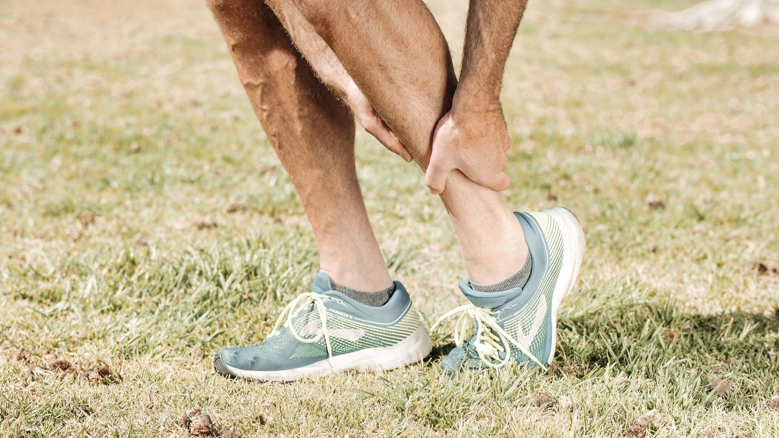 Man in running shoes holding his sore lower calf and Achilles tendon, a common sign of Achilles tendinitis treated with shockwave therapy in Hinsdale, IL
