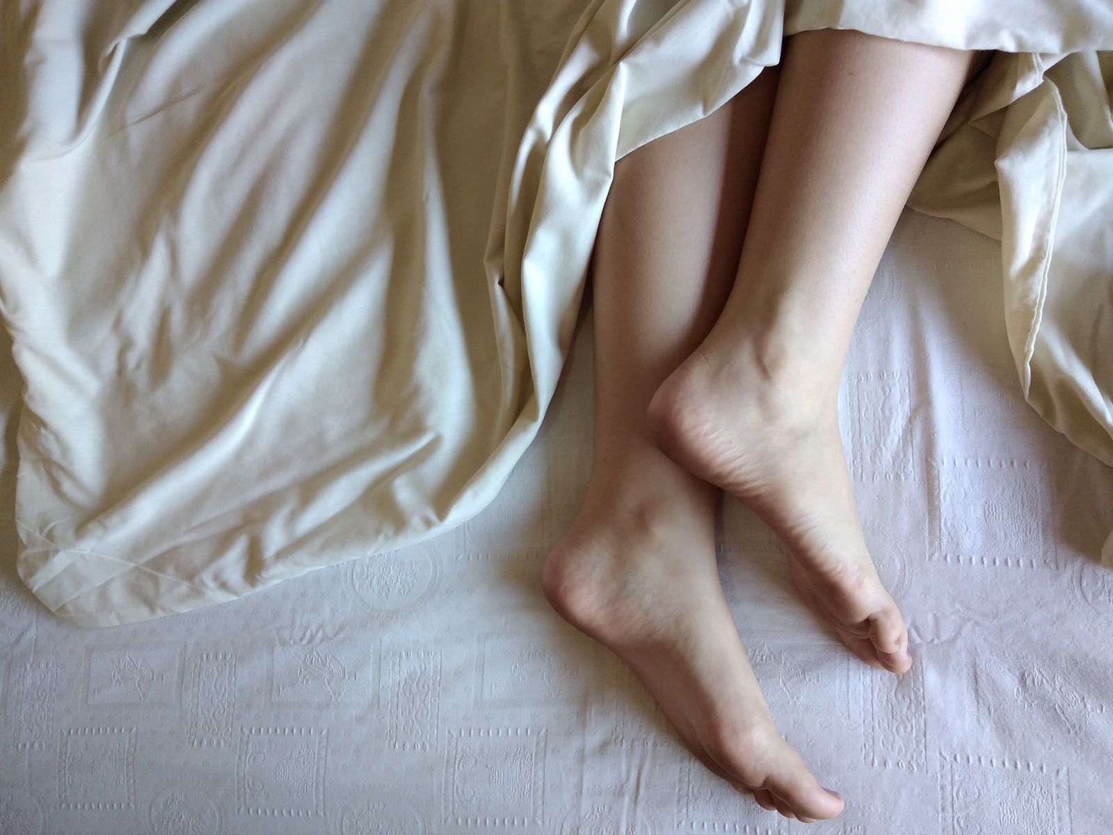 Bare feet resting on a bed in the morning, when the first steps out of bed often hurt most with plantar fasciitis, a symptom that tends to ease over a course of shockwave therapy in Hinsdale, IL