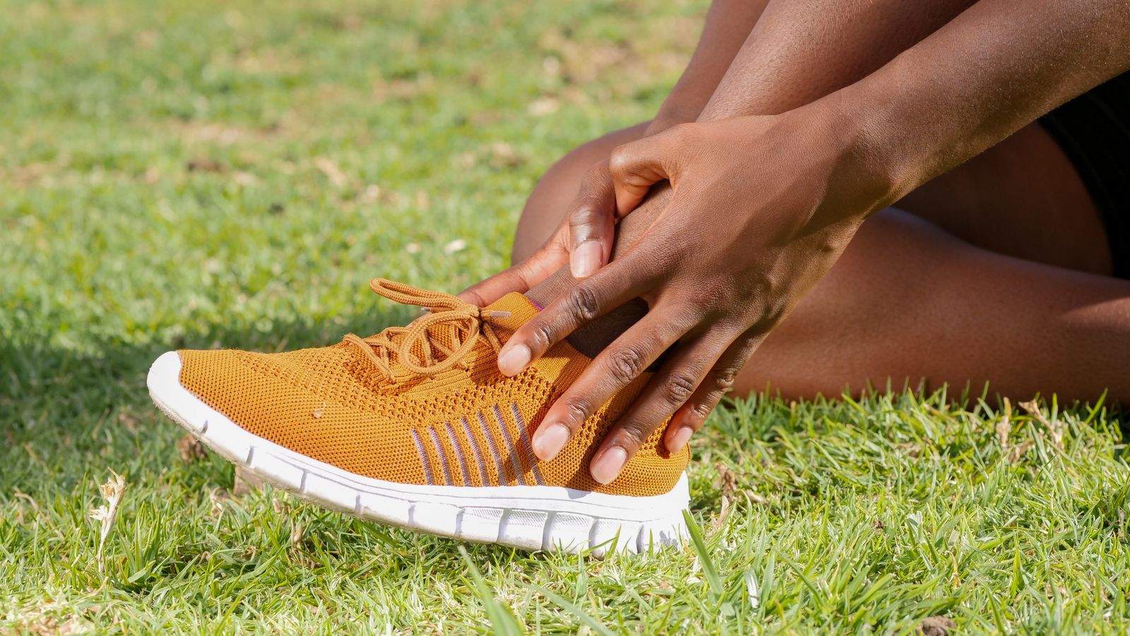 Person in orange sneakers holding a sore ankle and heel, the kind of stubborn heel pain that improves gradually over a course of shockwave therapy for plantar fasciitis in Hinsdale, IL