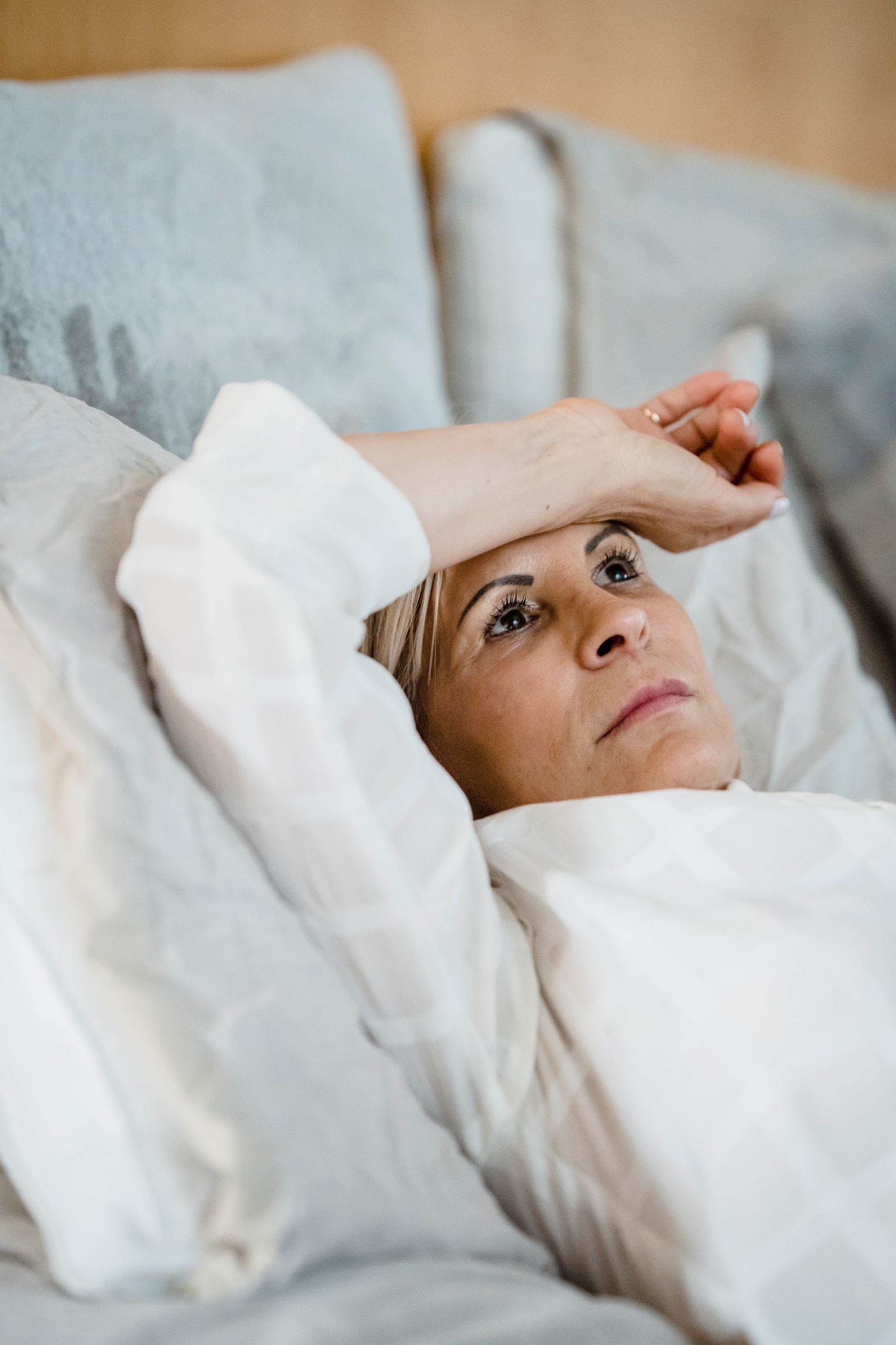 Mature woman lying awake in bed, the kind of sleepless night outer hip pain from hip bursitis or gluteal tendinopathy can cause, treated in Hinsdale, IL
