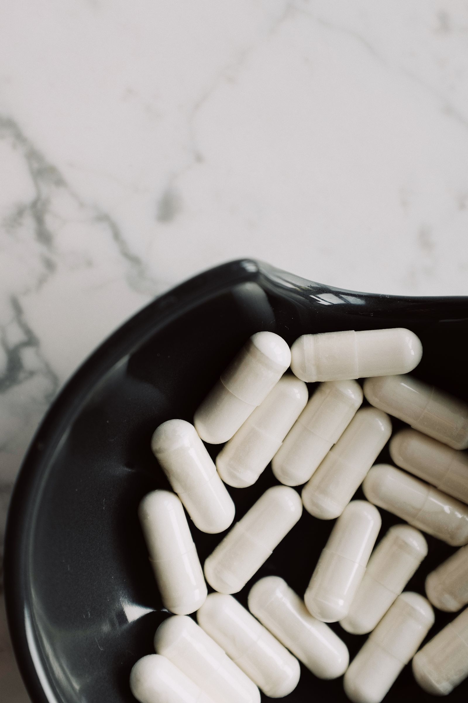 White supplement capsules in a black bowl for collagen and vitamin C tendon healing support, Hinsdale, IL